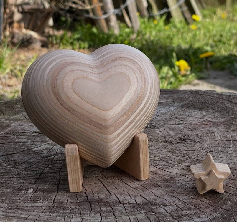 A heart-shaped wooden urn from Hart van Hout on a small stand, with a wooden star beside it